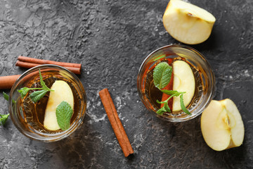 Tasty drink with cinnamon and apple slices in glasses on grey textured background