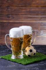 Photo of two glasses of beer, soccer ball on green grass
