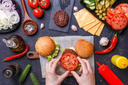 Image on top of two hamburgers, human hands and ingredients