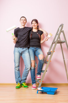 Photo of young woman and man with paint roller standing near staircase