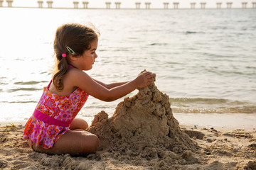 Fototapeta na wymiar Cute little girl playing with sand and building sandcastle on the beach in Dubai