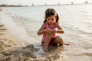 Fototapeta na wymiar Cute little girl playing with sand and building sandcastle on the beach in Dubai