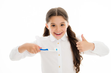 Girl cute long curly hair holds toothbrush white background. Child girl holds toothbrush with paste and shows thumbs up. Child school girl smart kid happy face cares hygiene. Brush teeth concept