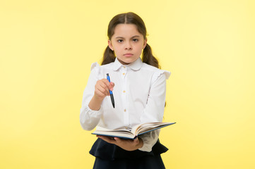 Girl cute serious face yellow background. Child girl school uniform clothes holds book and pen. Check my homework. Child school uniform smart kid done with homework. Check knowledge concept