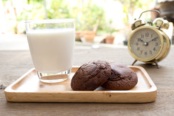 Homemade soft dark chocolate brownie cookies placed on a wooden plate with milk glass on wooden table. Behind cookies have gold vintage alarm clock