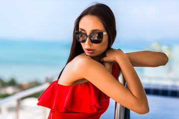 luxury beautiful girl in a branded swimsuit and glasses, in an expensive hotel on a tropical island, against a background of azure sea bay, on the terrace private infinity pool