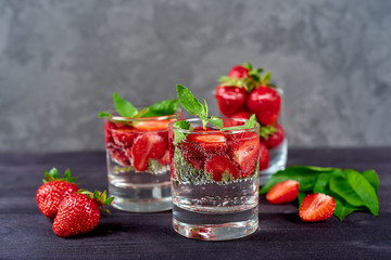 Lemonade drink of soda water, strawberry and mint leaves in glass on wooden table, copy space. Refreshing summer berry drink. Sparkling water drink  with slices of strawberry. Detox fruit in water