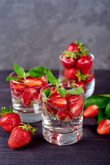 Lemonade drink of soda water, strawberry and mint leaves in glass on wooden table, copy space. Refreshing summer berry drink. Sparkling water drink  with slices of strawberry. Detox fruit in water
