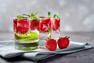 Fototapeta na wymiar Lemonade drink of soda water, strawberry and mint leaves in glass on napkin on gray stone concrete table, copy space. Refreshing summer berry drink with slices of strawberry. Detox fruit in water