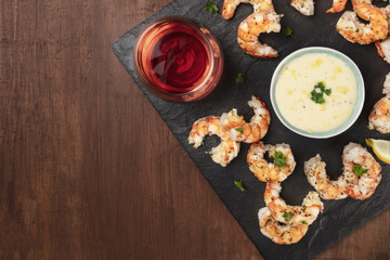 Obraz na płótnie Canvas Overhead photo of plate of cooked shrimps on a dark rustic background, with a sauce and a glass of wine, with copy space