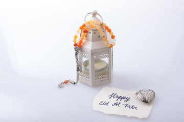 the word EID EL FITR   on torn paper beside lantern and prying beads