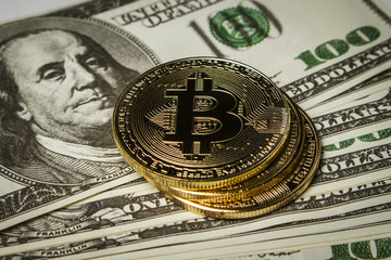 Three coins of bitcoin on a pack of dollars on a table