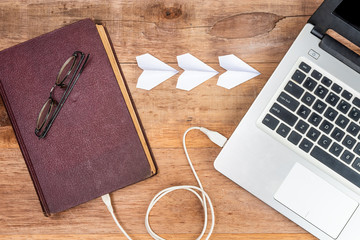 old book is connecting to a laptop with usb cable and three paper planes are symbol of loading, concept the evolution of book
