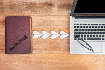 old book is connecting to a laptop with symbol of paper plane on wooden table, concept the evolution of book