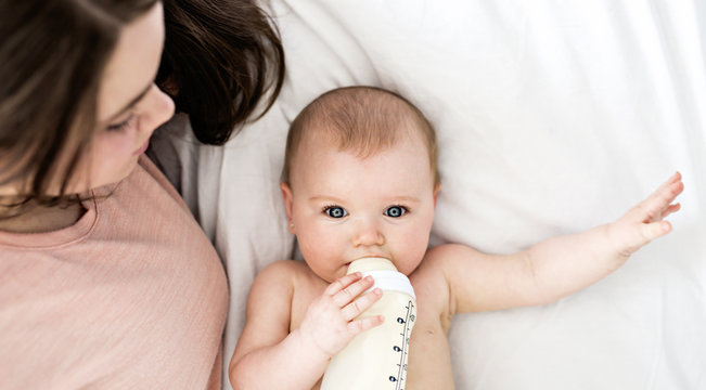 mother feeding baby with milk bottle in bed at home