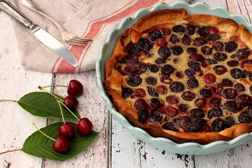 Fresh homemade cherry pie in blue baking pan with some raw cherries and fork and knife on linen kitchen towel, wooden background