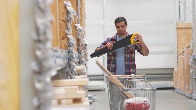 man in a shirt in a hardware store with a cart buys a saw