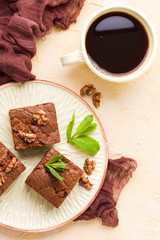 Brownie sweet chocolate dessert with walnuts and meant leaves on craft plate and cup of black coffee.