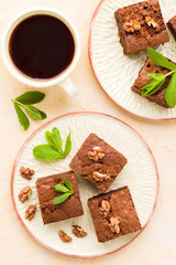Brownie sweet chocolate dessert with walnuts and meant leaves on craft plate and cup of black coffee.
