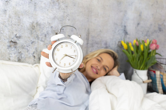 beautiful, blond woman in the morning is holding the alarm clock and ist getting ready for the day