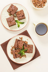 Brownie sweet chocolate dessert with walnuts and meant leaves on craft plate and cup of black coffee.