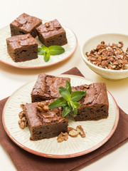 Brownie sweet chocolate dessert with walnuts and meant leaves on craft plate with copy space on pastel beige background.
