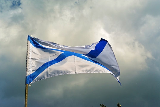 Naval flag of the Russian Navy St. Andrew on a storm cloudy blue sky background. Russian navy day concept.