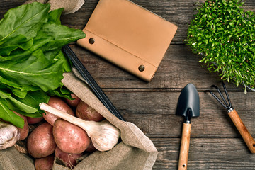 Red potatoes on burlap, garlic with greenery and a garden spade and rake on a wooden brown background