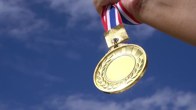 Winners Champion in success award concept : Businessman hands raised holding gold medals with ribbon against blue sky background to show success in sport or business, Slow motion video