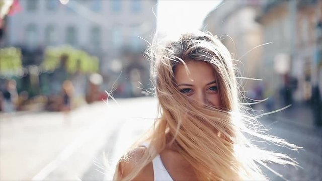 Charming young woman with a in a beautiful white dress with loose hair. Attractive young lady is rushing in the city-center, she turns to camera and smiles. Slow motion