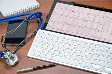 Doctor's table with tablet PC and electrocardiogram on it. Stethoscope and pen. Healthcare and medical concept.