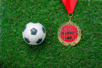 Table top view aerial image of decoration soccer or football season background.Flat lay accessories ball with gold medal on the artificial green grass wallpaper.Free space for design text and content.
