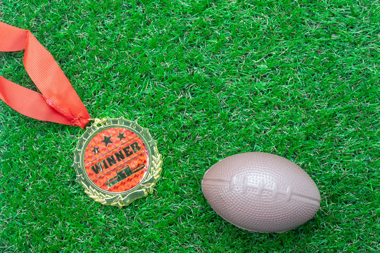 Table top view aerial image soccer or football season background.Flat lay accessories gold medal & american ball on the artificial green grass wallpaper.Free space for design text and content.