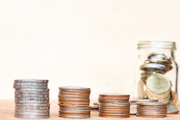 Glass of coin and four pole range of coins on vintage blurred background - Saving money concept.