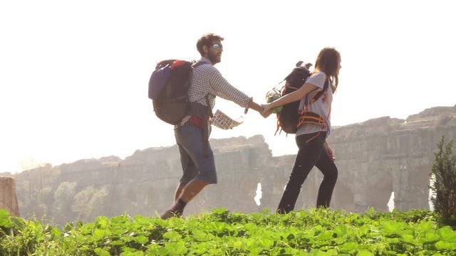 Young lovely couple backpackers tourists walking holding hands toward roman aqueduct arches in parco degli acquedotti park ruins in rome on romantic misty sunrise with guitar and sleeping bag slow