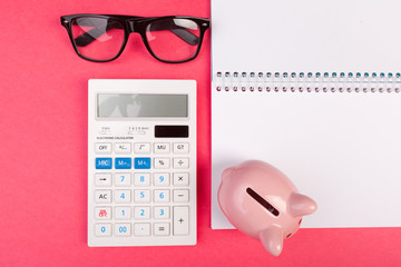 Piggy bank and calculator on color background, top view.