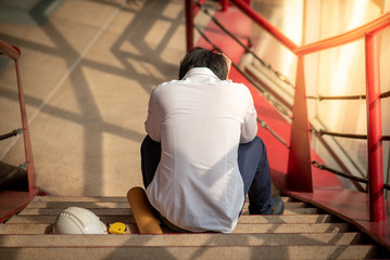 Engineer or Architect feeling stressed, worried and tired with his job while sitting on stair with...