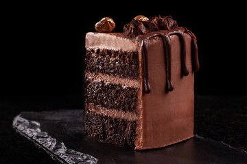 Piece of chocolate cake. Chocolate mousse cake slice on a black board, black background.