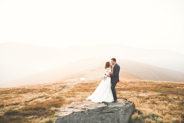 Fototapeta premium Young newly wed couple, bride and groom kissing, hugging on perfect view of mountains, blue sky