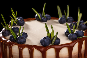 Chocolate cake with blueberries on a black background, decorated with small green leaves and fresh berries