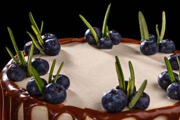 Chocolate cake with blueberries on a black background, decorated with small green leaves and fresh berries