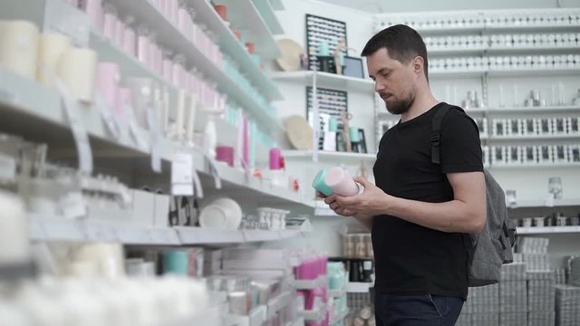 Regular guy choosing new aroma candles for his apartment. Man is holding two different candles and can't decide.