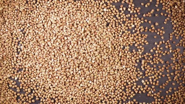 A pile of buckwheat groats falls on a gray background from under the camera slow motion
