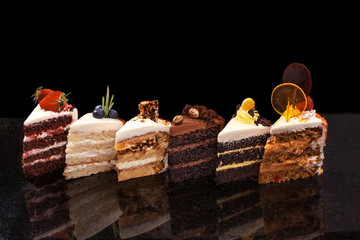 Izabrani veliki komadi različitih kolača: čokolada, maline, jagode, orašasti plodovi, borovnice. Komadi kolača na crnom stolu.