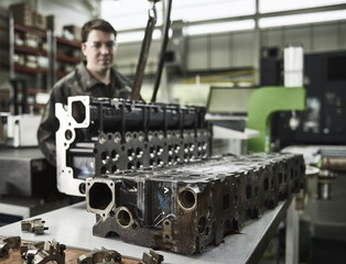 Worker in metalworking factory lifting cylinder head with crane