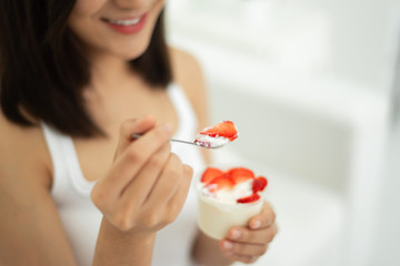Beautiful woman eating strawberries with yogurt.