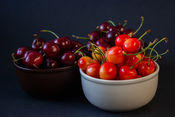 Ripe juicy cherries on a black background. Delicious cherries in plates.