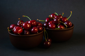 Ripe juicy cherries on a black background. Delicious cherries in plates.