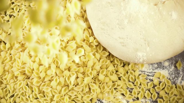 Slow motion pasta mini conchiglie rigate strew next to the dough ball on the flour