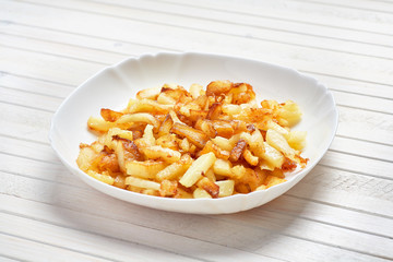 Fried potatoes in a white plate on a white wooden background.